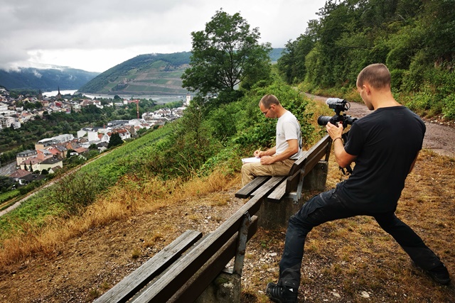 Ein Kameramann filmt den Botaniker, der auf einer Bank am Hang mit Blick auf den Oberrhein sitzt und die geernteten Samen notiert.